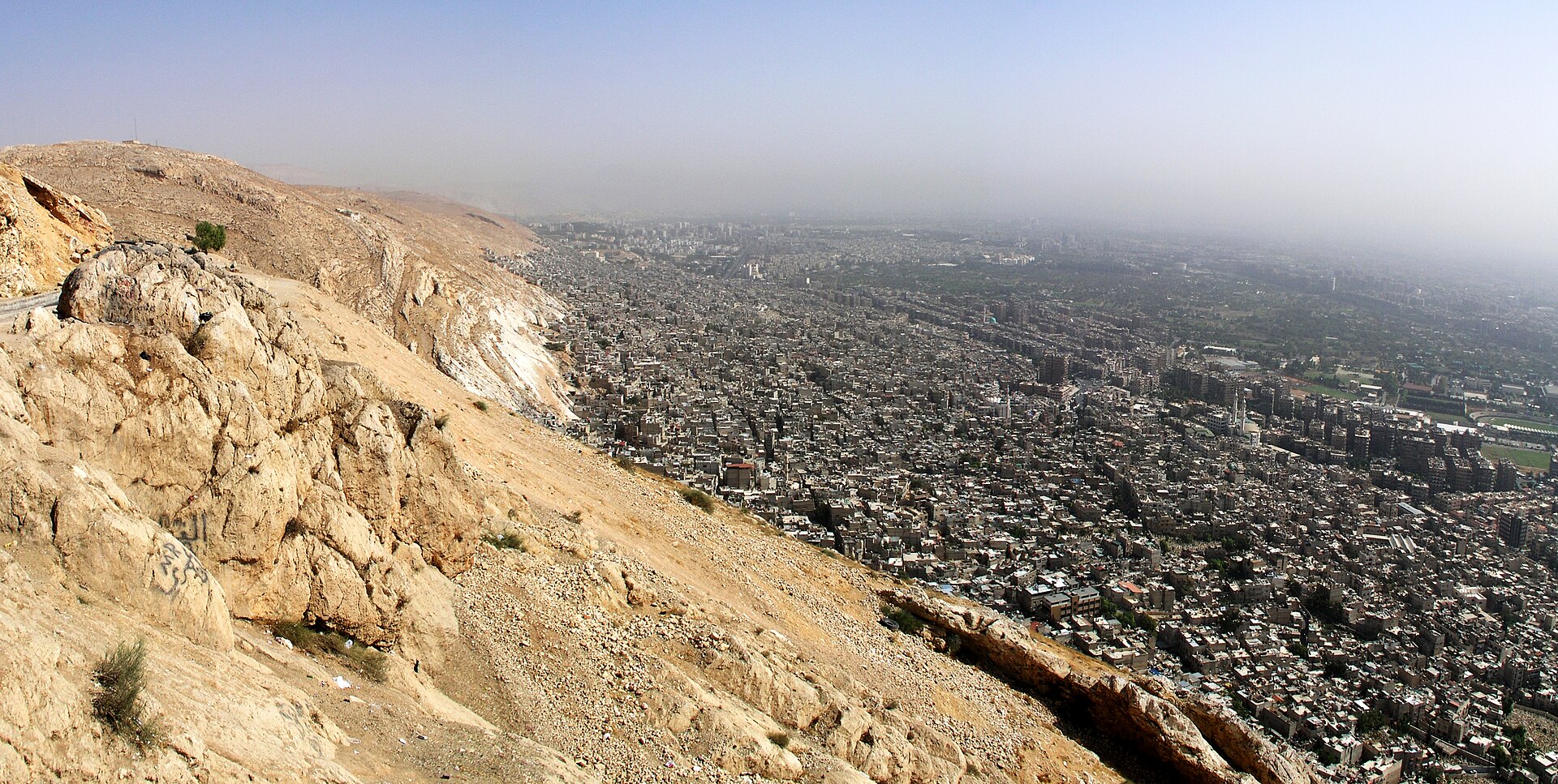 Damascus seen from the slopes of Mount Qasioun — the dense city below the arid mountain edge that frames Al Adawi Park